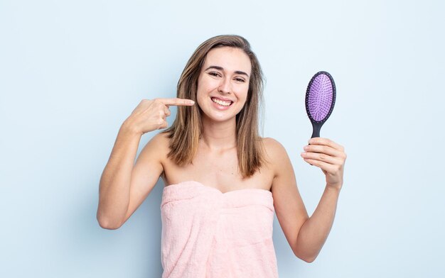 Jeune jolie femme souriante en toute confiance pointant vers son large sourire. concept de brosse à cheveux