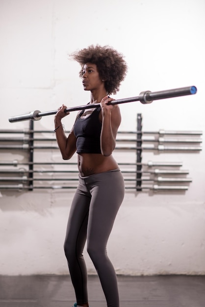 Jeune jolie femme de sport afro-américaine dans la salle de fitness soulevant une barre vide