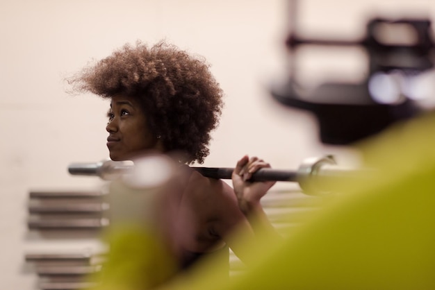 Jeune jolie femme de sport afro-américaine dans la salle de fitness soulevant une barre vide