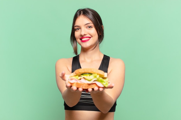 Jeune jolie femme sportive expression heureuse et tenant un sandwich