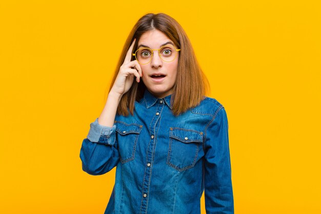 Jeune jolie femme à la surprise, bouche bée, choquée, réalisant une nouvelle pensée, idée ou concept contre le mur jaune