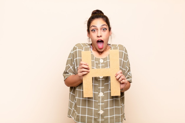 Jeune jolie femme surprise, choquée, émerveillée, tenant la lettre H de l'alphabet pour former un mot ou une phrase.