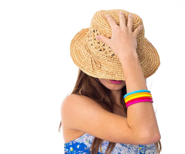 Jeune jolie femme en T-shirt bleu et short avec des bracelets colorés cachant son visage avec le chapeau