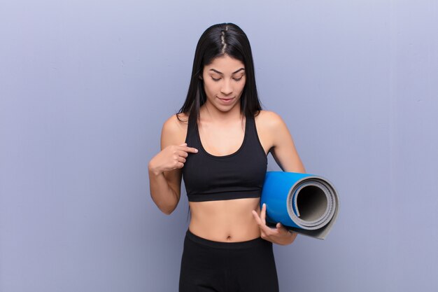 Jeune jolie femme avec un tapis de yoga contre le mur de ciment