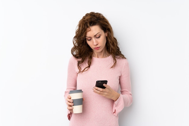 Jeune jolie femme tenant un café à emporter et un téléphone portable