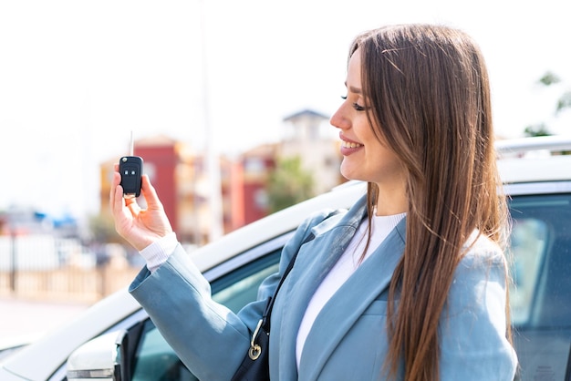 Jeune jolie femme tenant des clés de voiture à l'extérieur avec une expression heureuse