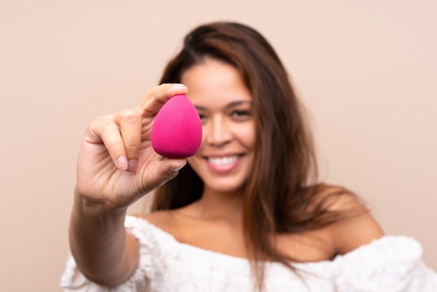 Jeune jolie femme tenant des cosmétiques sur un mur isolé