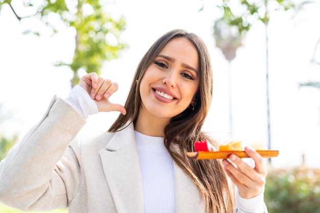 Jeune jolie femme tenant du sashimi à l'extérieur fière et satisfaite