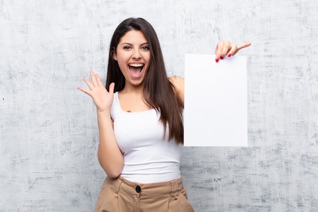 Jeune jolie femme tenant une feuille de papier contre le mur de ciment grunge