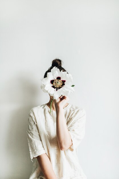 Jeune jolie femme tenant une fleur de pivoine blanche sur une surface blanche