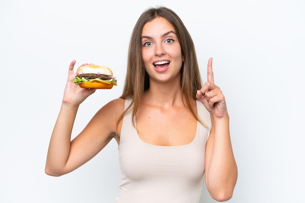 Jeune jolie femme tenant un hamburger isolé sur fond blanc pointant vers le haut une bonne idée