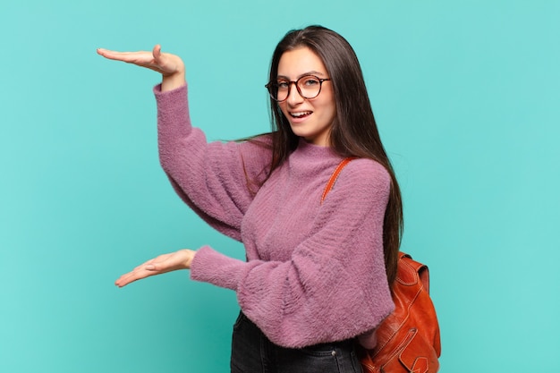 jeune jolie femme tenant un objet avec les deux mains sur l'espace de copie latéral, montrant, offrant ou faisant la publicité d'un objet. concept d'étudiant