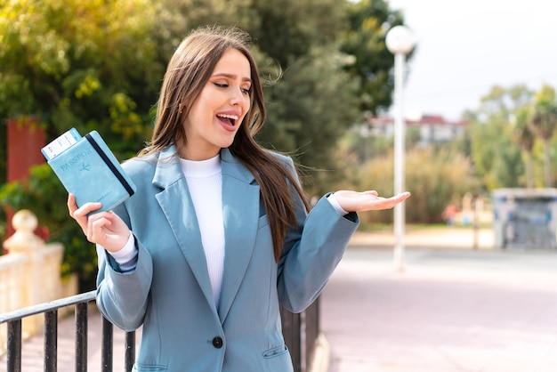 Jeune jolie femme tenant un passeport à l'extérieur avec une expression faciale surprise