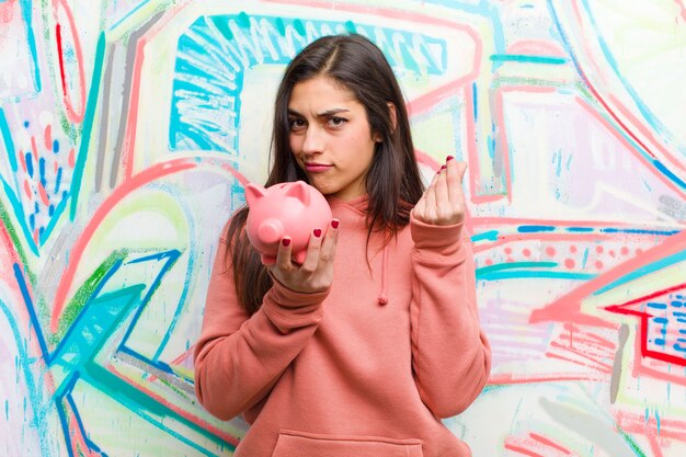 Jeune jolie femme avec une tirelire contre le mur de graffitis