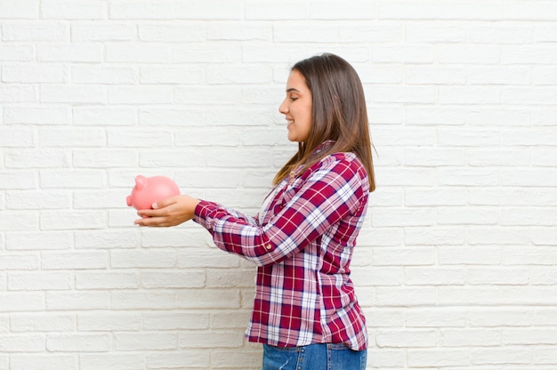 Jeune jolie femme avec une tirelire contre la texture de mur de briques