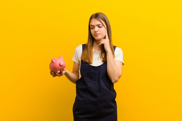 Jeune jolie femme avec une tirelire sur fond orange