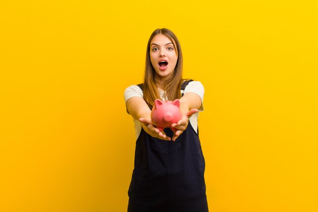 Jeune jolie femme avec une tirelire sur fond orange