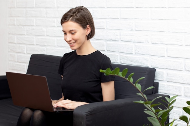 Jeune jolie femme travaillant sur un ordinateur portable dans un canapé à l'intérieur de la maison.