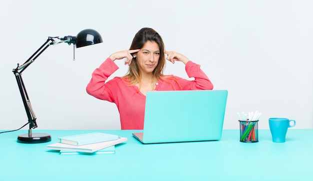 Jeune jolie femme travaillant avec un ordinateur portable, se sentant confuse ou douteuse, se concentrant sur une idée, réfléchissant bien, cherchant à copier de l'espace sur le côté