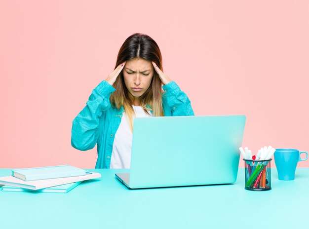 Jeune jolie femme travaillant avec un ordinateur portable, stressée et frustrée, travaillant sous pression avec maux de tête et troublée par des problèmes