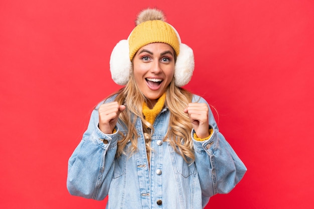 Jeune jolie femme uruguayenne portant des manchons d'hiver isolés sur fond rouge célébrant une victoire en position de vainqueur