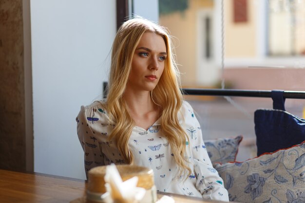 Jeune jolie femme vêtue d'une robe blanche se reposant dans un café