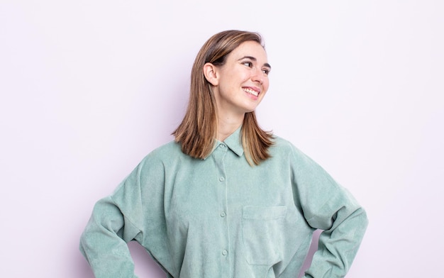 Jeune jolie fille à l'air heureuse, gaie et confiante, souriante fièrement et regardant de côté avec les deux mains sur les hanches