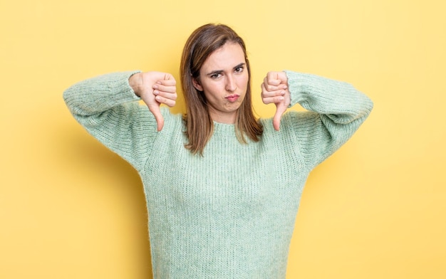 Jeune jolie fille à l'air triste, déçue ou en colère, montrant les pouces vers le bas en désaccord, se sentant frustrée