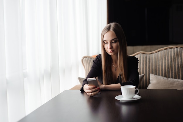 Jeune jolie fille assise seule près d'une grande fenêtre