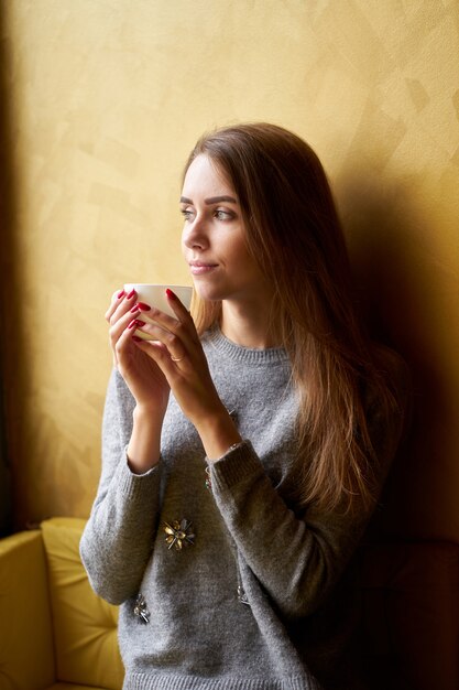 Jeune jolie fille aux cheveux longs, boire du café ou du thé dans le café.