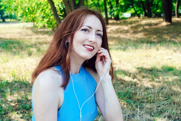 Jeune jolie fille aux cheveux rouges écoute de la musique en été filaire.