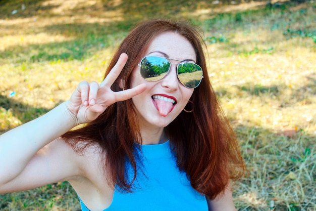 Jeune jolie fille aux cheveux rouges regardant la caméra, portant des lunettes de soleil.