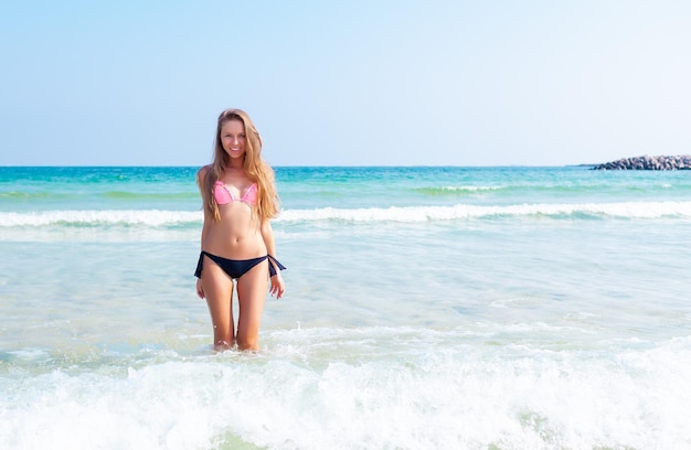 Jeune jolie fille blonde avec un corps de sport parfait en bikini sur la plage tropicale d'été