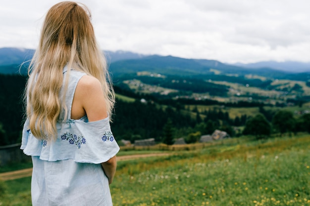 Jeune jolie fille blonde élégante en robe romantique bleue posant sur un paysage pittoresque