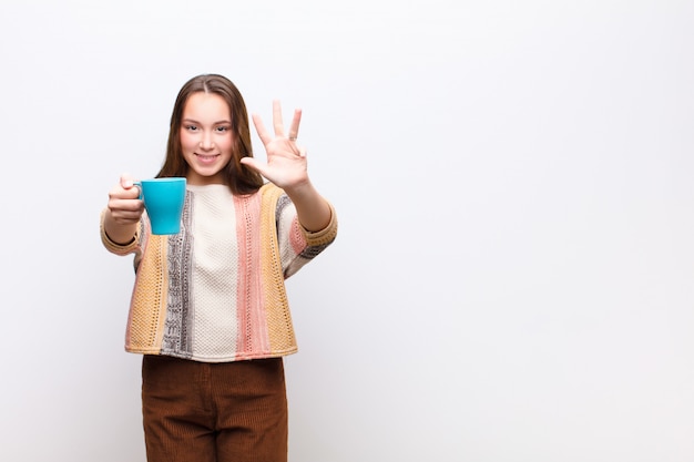 Jeune jolie fille blonde avec une tasse de café contre le mur blanc