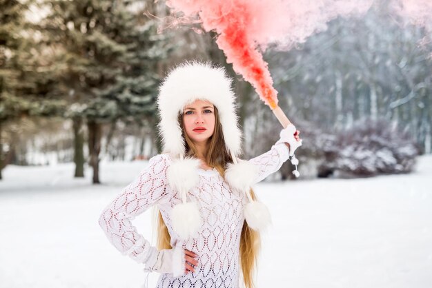 Jeune jolie fille avec une bombe fumigène de couleur rouge à la main en journée d'hiver