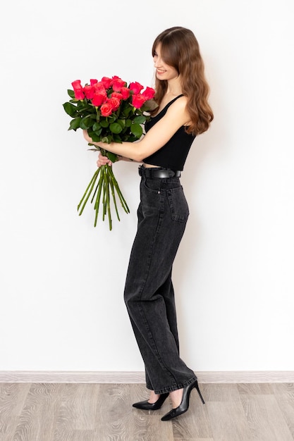Jeune jolie fille avec un bouquet de roses rouges en pleine croissance sur fond blanc vue latérale Le concept de bonheur joie et célébration