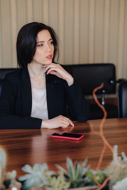 Jeune jolie fille émotionnelle en vêtements de style d&#39;affaires assis au bureau avec téléphone