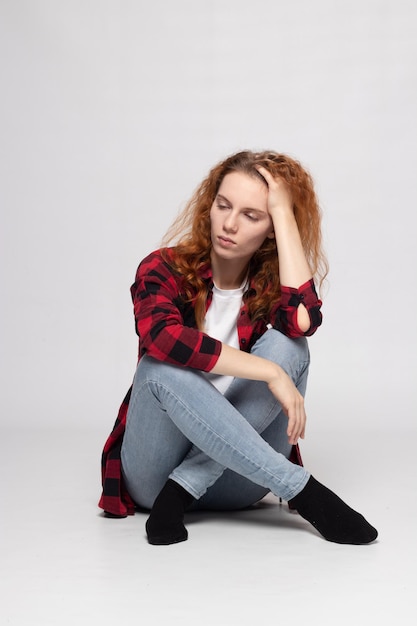 Une jeune jolie fille est assise sur un fond blanc dans une chemise à carreaux