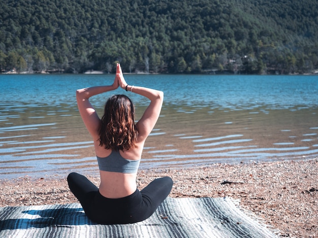 Jeune et jolie fille faisant du yoga en plein air, à côté d'un lac, entouré par la nature. Concept de vie saine.