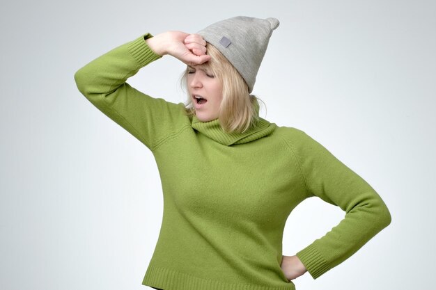 Photo jeune jolie fille fatiguée portant un pull vert et un chapeau bâillant les yeux fermés