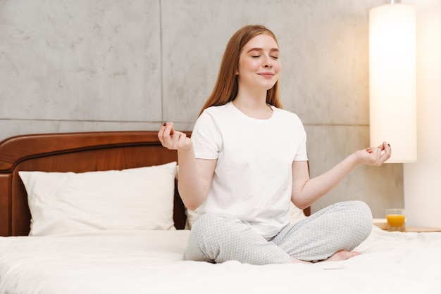 jeune jolie fille heureuse à l'intérieur à la maison dans la chambre à méditer sur le lit.