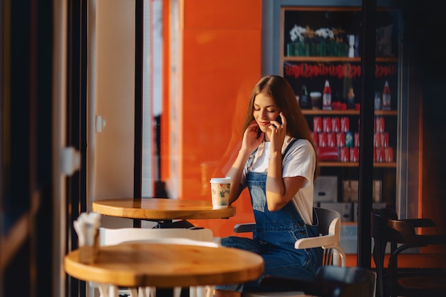 Jeune jolie fille jolie au café avec café et téléphone à rayons du matin