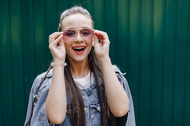 Jeune jolie fille jolie dans des vêtements en denim dans des verres sur un simple fond vert foncé avec place pour le texte.