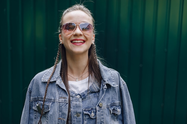 Jeune jolie fille jolie dans des vêtements en denim dans des verres sur un simple fond vert foncé avec place pour le texte.