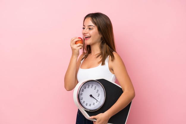 Jeune jolie fille avec machine de pesage et avec une pomme sur rose isolé