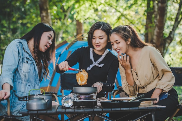 Jeune jolie fille a mis un œuf sur une casserole en camping avec ses amis en train de cuisiner un repas facile dans un parc naturel Ils aiment discuter et rire avec plaisir ensemble copiez l'espace