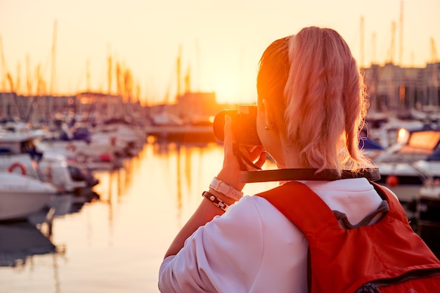 Jeune jolie fille prend une photo d'une baie avec des yachts au coucher du soleil