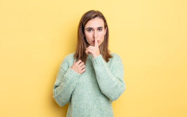 jeune jolie fille à la recherche sérieuse et croisée avec le doigt appuyé sur les lèvres exigeant le silence ou la tranquillité, gardant un secret