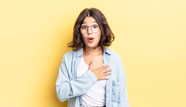 Jeune jolie fille se sentant choquée et surprise, souriante, prenant la main à cœur, heureuse d'être la seule ou de montrer de la gratitude